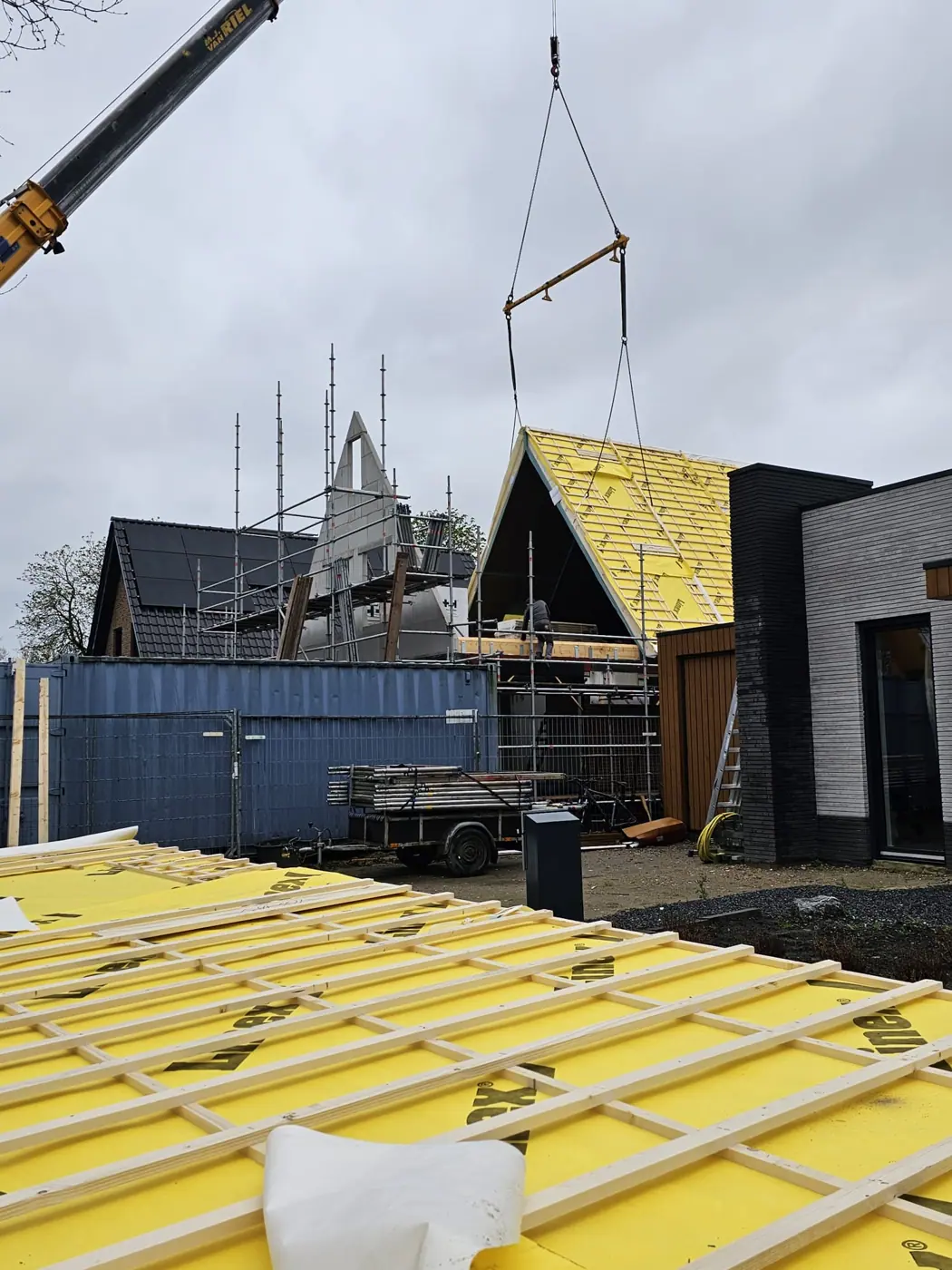 Dakplaten met panlatten liggen klaar terwijl een kraan een dakdeel hijst