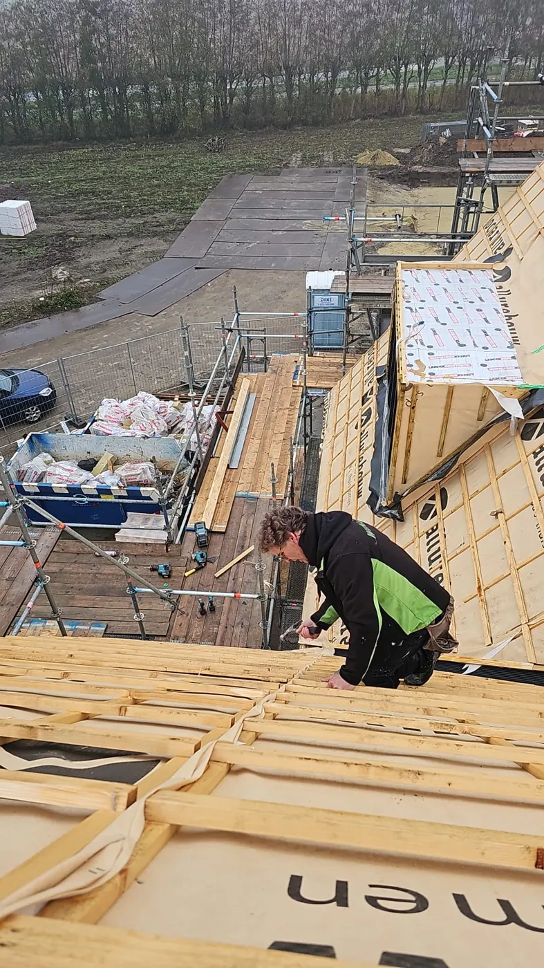 Vakman aan het werk tussen de panlatten op een schuin dak, met de steiger ernaast