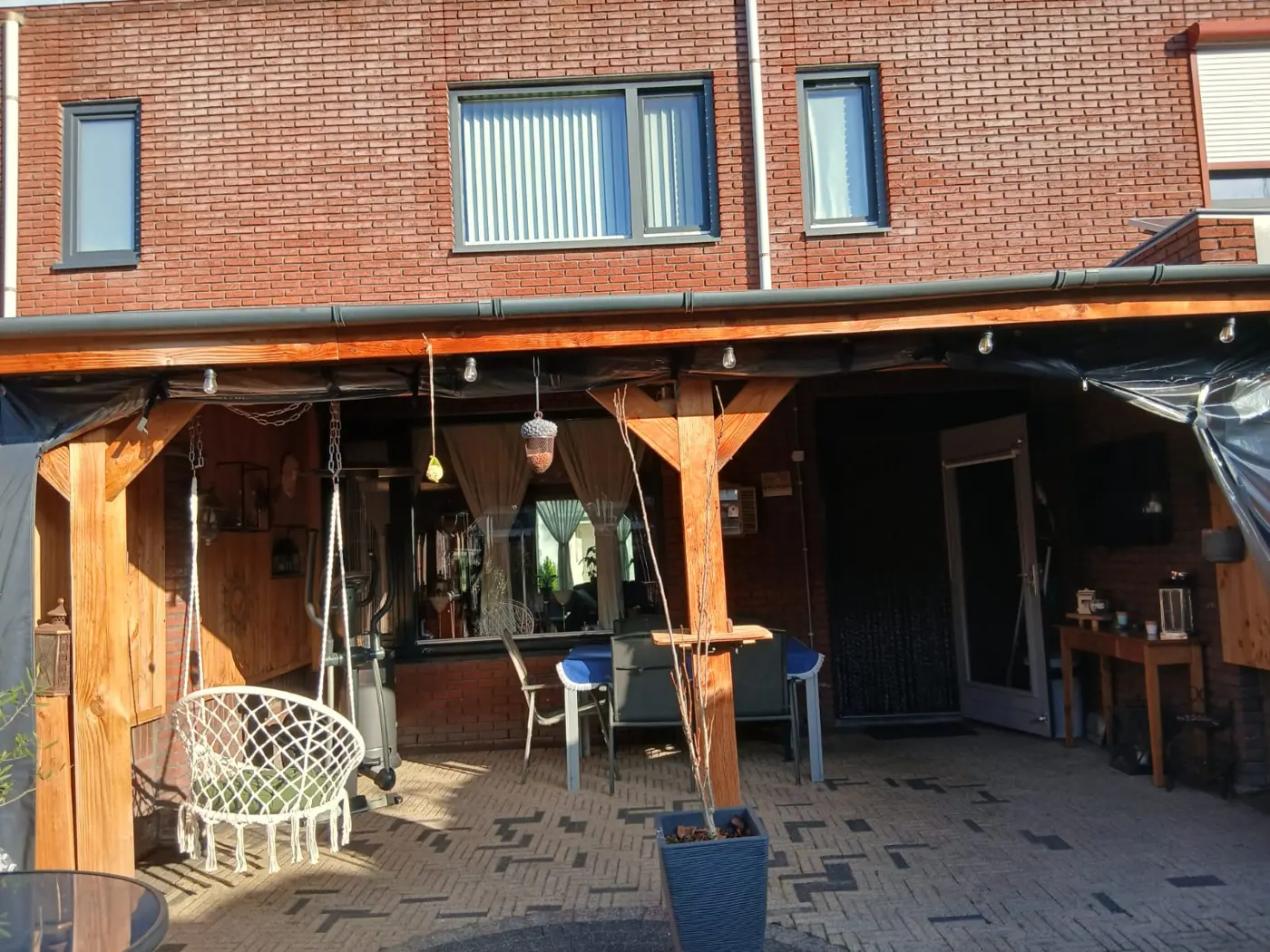 Houten overkapping met plat dak tegen de achtergevel, met zitplek en hangstoel