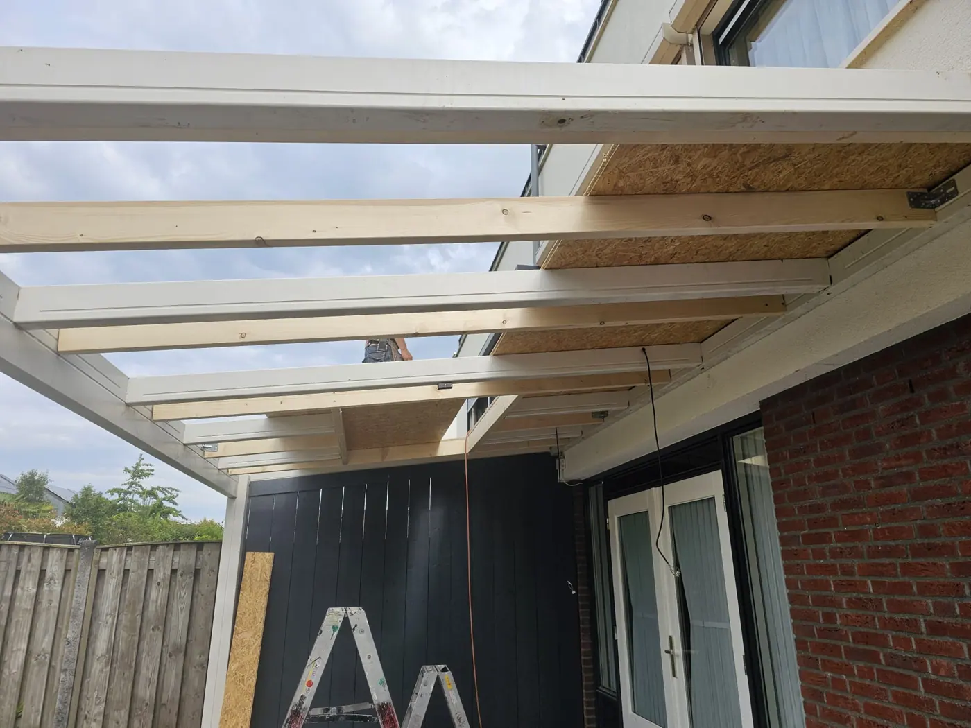 Overkapping in opbouw met wit geschilderde balken tegen de gevel