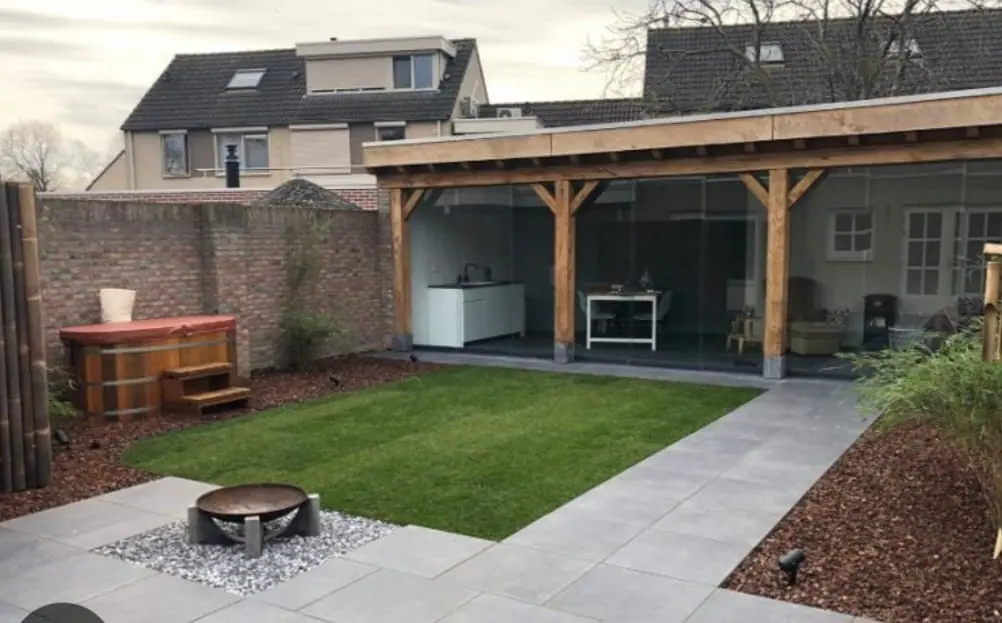Tuin met gazon, tegelpad, vuurschaal en een overkapping met glazen wanden
