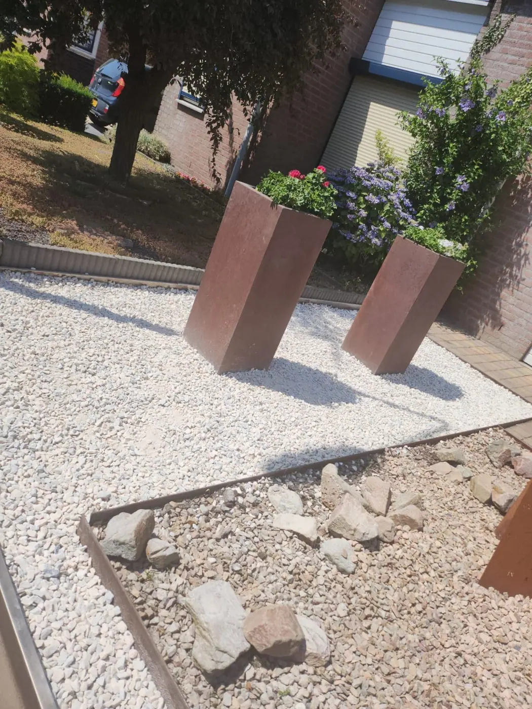 Voortuin met wit grind, cortenstalen plantenbakken en keien