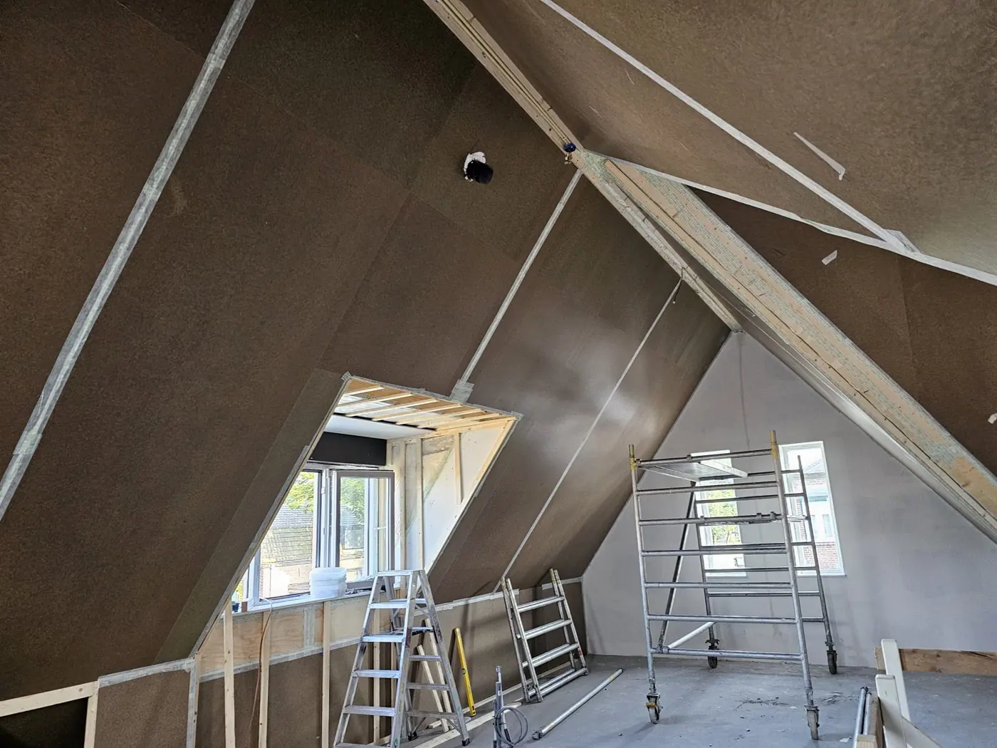 Schuine dakvlakken bekleed met plaatmateriaal, met een dakkapel en rolsteiger
